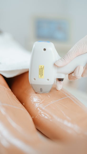 Image of a professional moving technician wearing disposable gloves, using a handheld ultrasound or scanner device on a person's bare leg, which is covered with a protective plastic sheet. The scene takes place indoors, with a blurred background that suggests a clinical or home environment, and a monitor or screen visible behind the equipment. This image illustrates the careful handling and preparation involved in house removals or home relocation services offered by Man with Van Hither Green, highlighting the importance of proper procedures during packing, furniture transport, or health and safety checks in the moving process.
